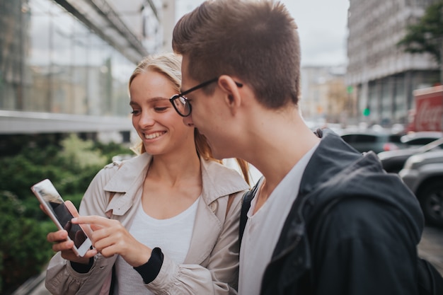 Pareja o amigos riendo divertido y divirtiéndose con un teléfono inteligente en una calle de la gran ciudad.