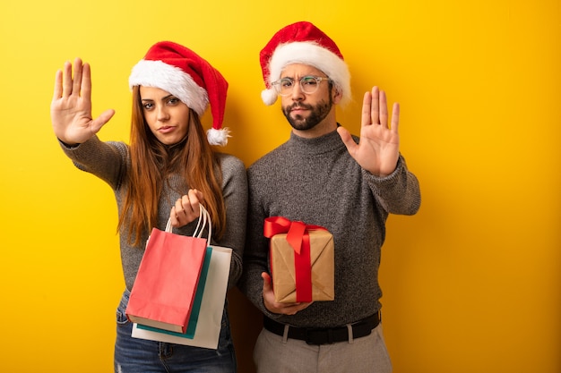 Pareja o amigos sosteniendo regalos y bolsas de compras poniendo la mano en frente