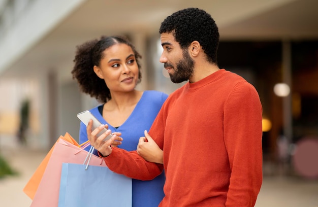 Pareja de Oriente Medio usando teléfonos inteligentes de compras en línea de pie en el supermercado