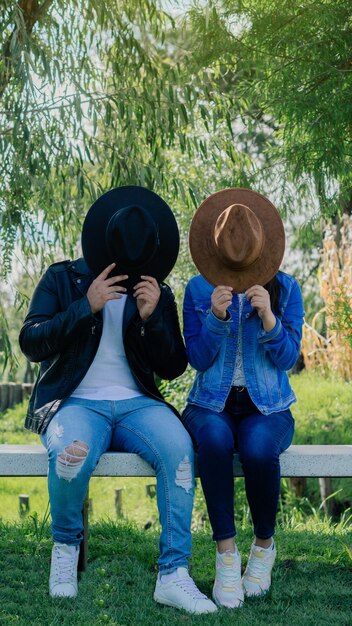 Pareja en un parque cubriéndose la cara con un sombrero.