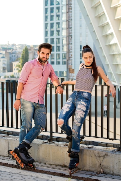 Pareja en patines al aire libre. Personas de pie en el fondo de la ciudad. Joven, audaz y con estilo.