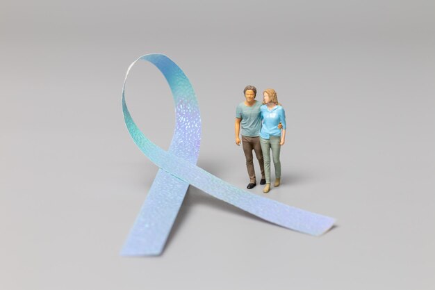 Pareja de personas en miniatura de pie delante de cintas, concepto del día mundial del cáncer