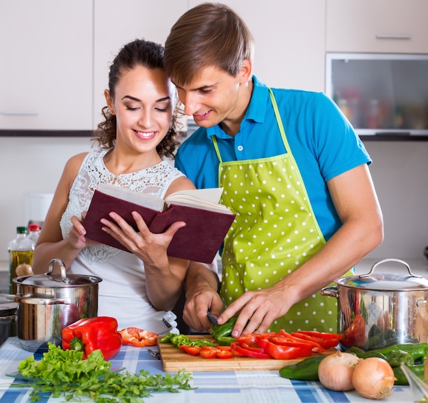 Pareja de pie con libro de cocina en la cocina