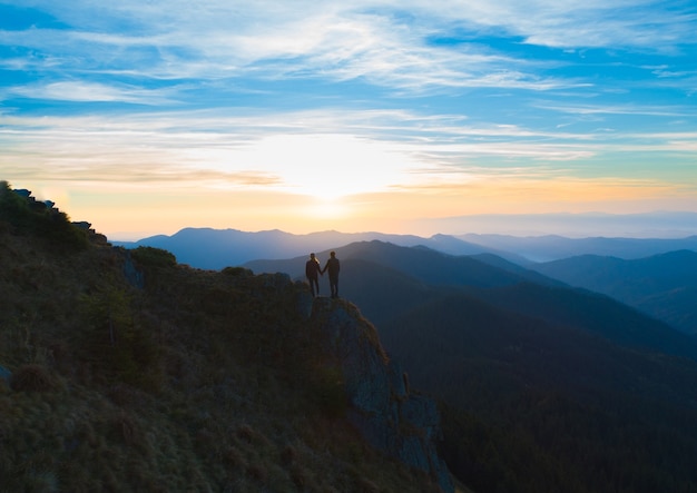 La pareja de pie en la montaña en el fondo del amanecer