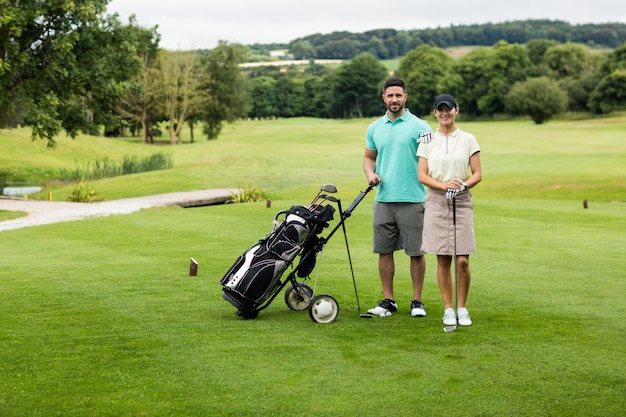 Pareja de pie con palo de golf y bolsa en campo de golf