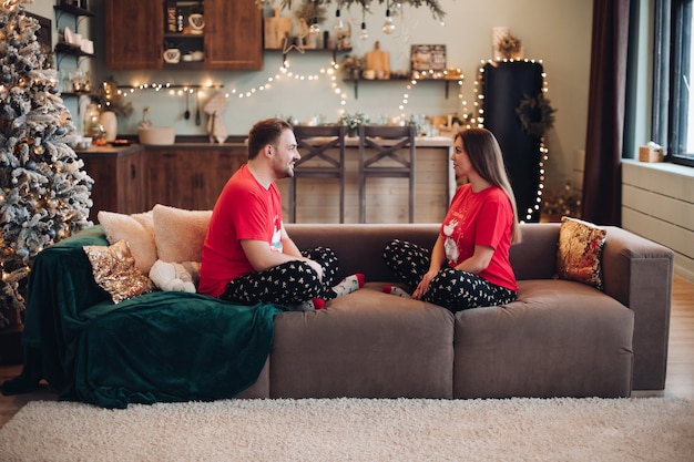 Pareja en pijama de Navidad similar sentado en el sofá