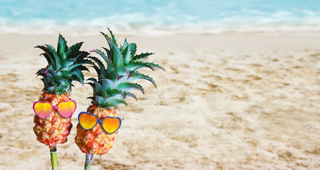 Pareja piñas con gafas de sol en la arena en la playa Hola verano concepto