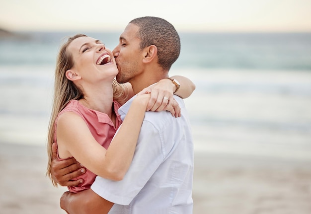 Pareja de playa amor abrazo y beso para vacaciones de verano matrimonio feliz y estilo de vida juntos Mujer riendo hombre juguetón y relación interracial disfrutando de vacaciones de viaje por el océano vacaciones y felicidad