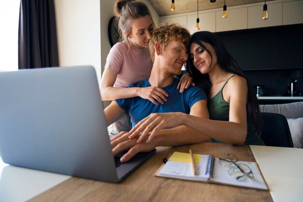 Foto pareja poliamorosa en casa trabajando en laptop
