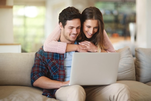 Pareja portátil y abrazo en casa en el sofá para película película y transmisión en línea Hombre mujer y tecnología con sonrisa en casa sala de estar en el sofán para redes sociales internet y suscripción a sitio web