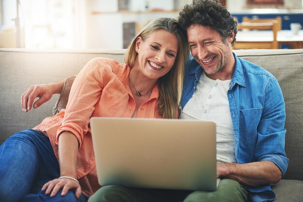 Pareja portátil y sofá en casa feliz y relajarse para elegir con programa de cine o suscripción de transmisión personas maduras hombre y mujer con computadora en el sofá en la sala de estar con abrazo película y sonrisa