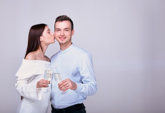 Pareja posando con copas de champán y niña lo besa en la mejilla sobre fondo blanco.