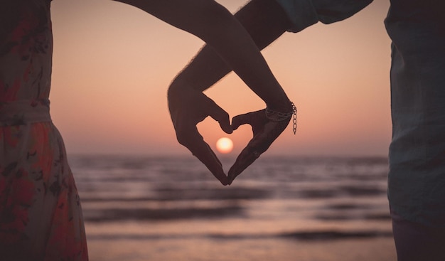 Pareja posando un corazón mostrando una hermosa puesta de sol