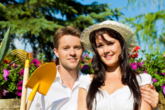 Pareja posando delante de flores con herramientas de jardinería