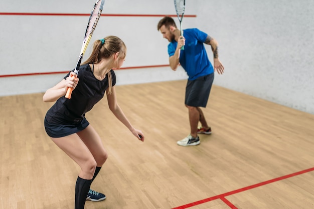 Pareja con raquetas de squash, club de entrenamiento de interior