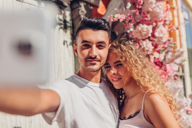 Pareja de raza mixta en el amor tomando selfie en smartphone caminando en la ciudad. Feliz hombre árabe y mujer blanca en cita romántica