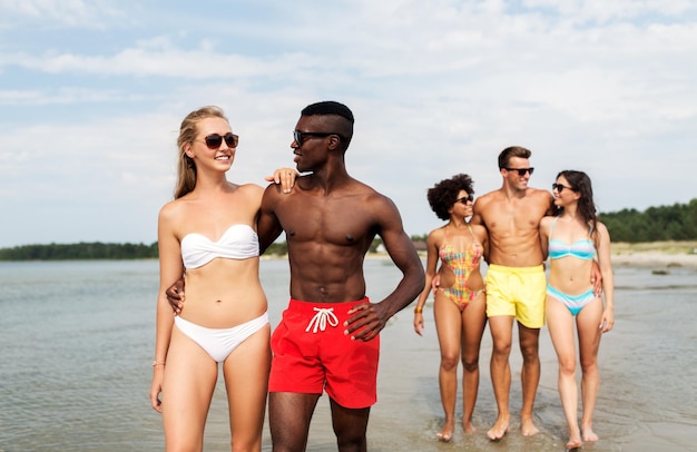 Una pareja de raza mixta caminando por la playa con amigos.