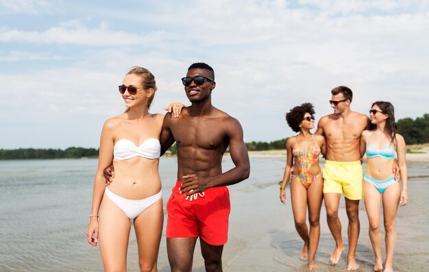 Una pareja de raza mixta caminando por la playa con amigos.