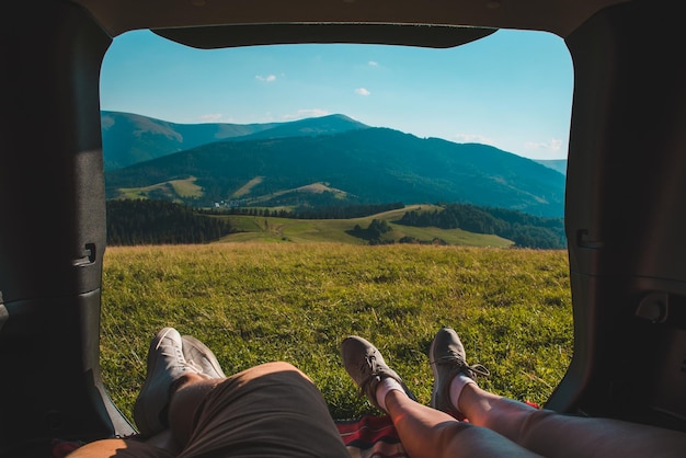 Pareja recostada en el baúl del auto con hermosa vista de las montañas