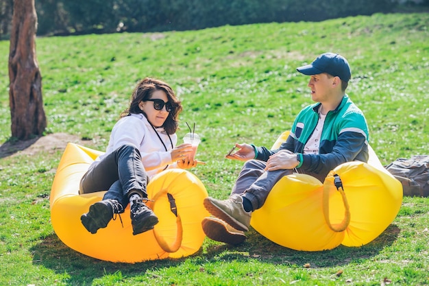 Pareja recostada sobre un colchón inflable en el parque de la ciudad en un día soleado hablando y charlando