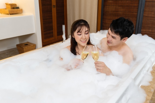 Pareja relajada bebiendo vino de cristal mientras disfruta de un baño de burbujas en una bañera