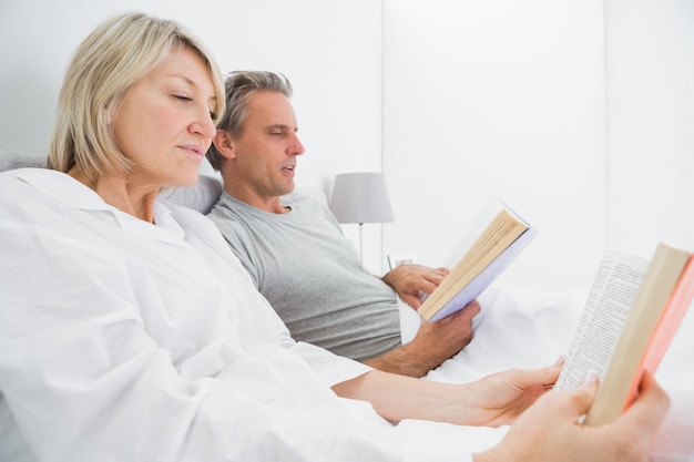 Pareja relajada leyendo libros en la cama