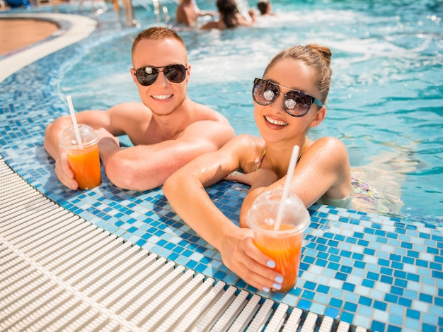 Pareja relajante en la piscina del complejo, tomando cócteles.