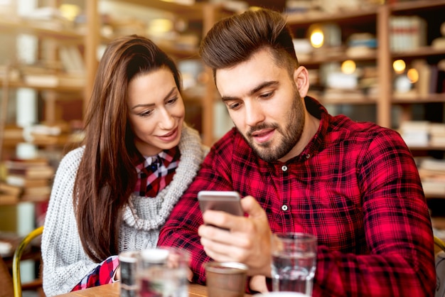 Pareja en el restaurante mirando el teléfono inteligente.