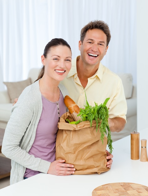 Pareja riendo de pie en la cocina con bolsas de compras