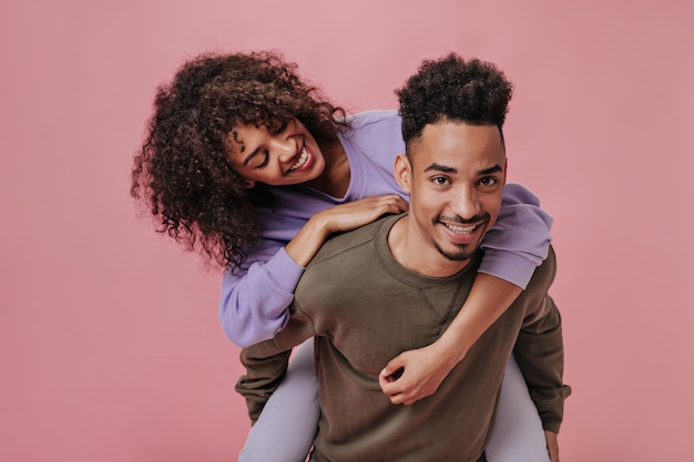 Pareja rizada sonriendo y divirtiéndose en la pared rosa