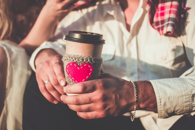 Pareja romántica abrazándose mientras hace un picnic Taza de café acogedora manga tejida con corazón rojo de fieltro