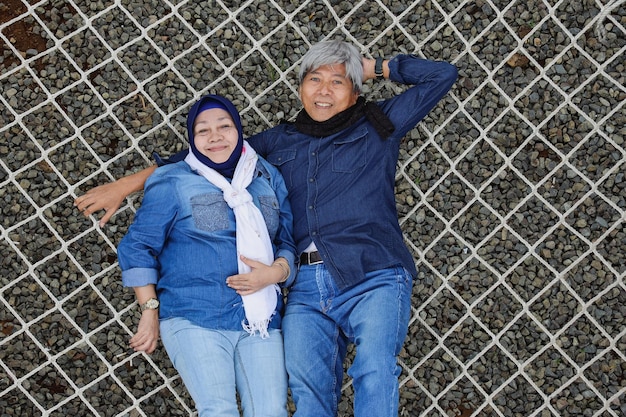 Pareja romántica de ancianos asiáticos acostados en una red estética con las rocas debajo Cónyuge feliz y saludable