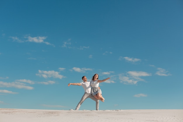 Pareja romántica bailando en el desierto de arena en el cielo azul