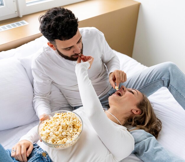 Pareja romántica comiendo palomitas de maíz en la cama en casa