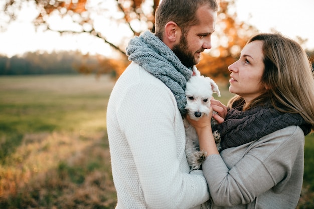 Pareja romántica con divertida mascota abrazando en el campo en puesta de sol en verano.