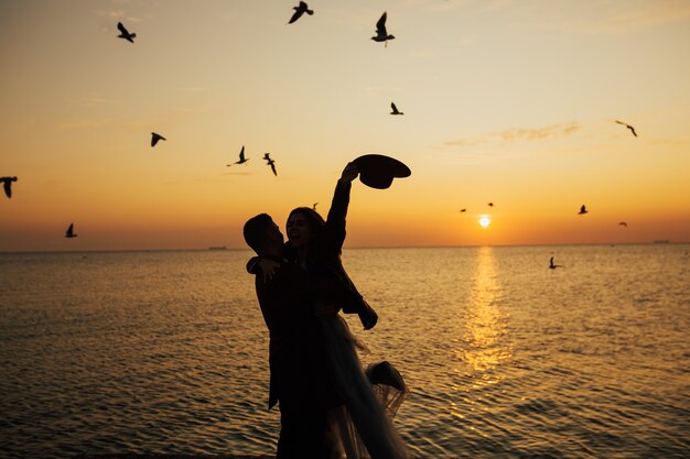 Pareja romántica se encuentra en la orilla del mar bajo los rayos dorados del sol y pasa tiempo juntos, disfrutando de la hermosa puesta de sol.