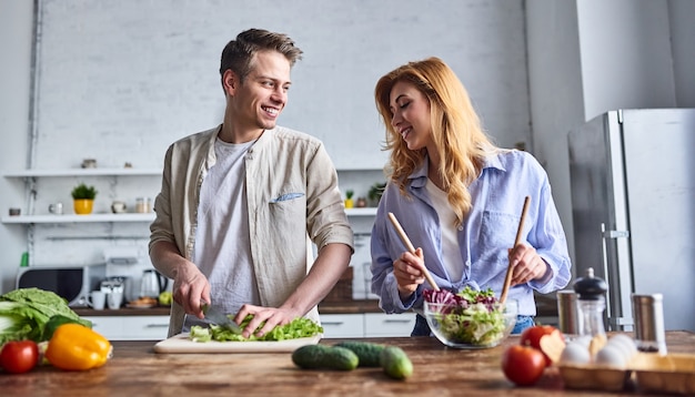 Pareja romántica está cocinando en la cocina. Hombre guapo y mujer joven atractiva se divierten juntos mientras hacen ensalada. Concepto de estilo de vida saludable.