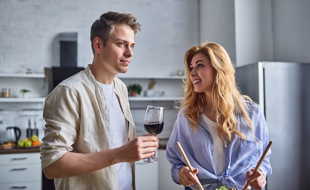 Pareja romántica está cocinando en la cocina. Hombre guapo y mujer joven atractiva se divierten juntos mientras hacen ensalada. Concepto de estilo de vida saludable.