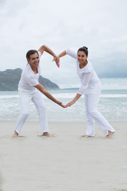 Foto pareja romántica haciendo corazón con las manos en la playa