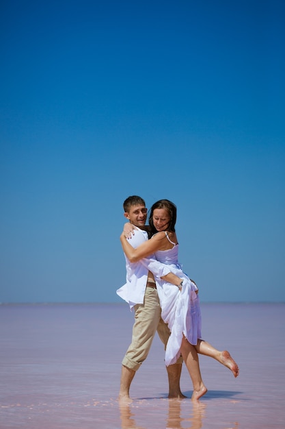 Una pareja romántica, un hombre y una mujer vestidos de blanco bailan en un lago rosa en un día soleado,
