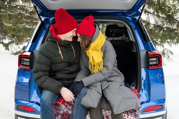 Pareja romántica joven inconformista abrazándose mientras está sentado en el maletero del coche. Amor, San Valentín y vacaciones.