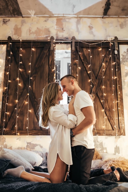 Pareja romántica pasando tiempo antes de Año Nuevo en casa con guirnaldas. Mujer joven y hombre guapo abrazo, beso. Tiempo de Navidad. Pareja feliz en año nuevo