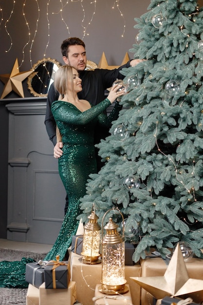 Pareja romántica de pie cerca del árbol de Navidad con ropa magnífica