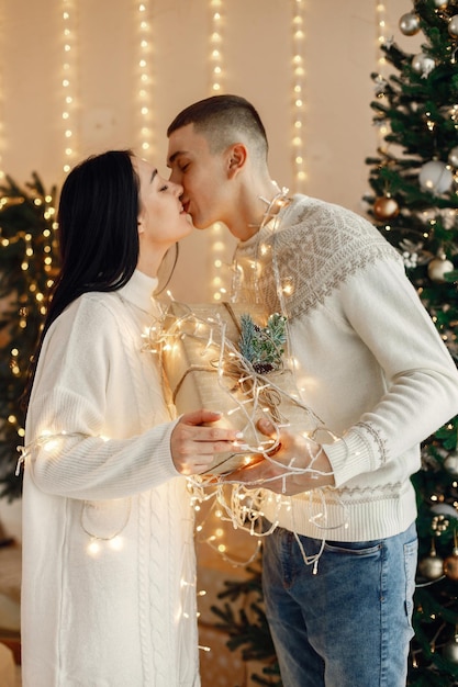 Pareja romántica de pie cerca del árbol de Navidad y sosteniendo una caja de regalo