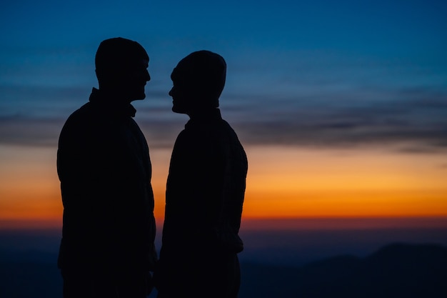 La pareja romántica de pie en el fondo del paisaje de montaña con una puesta de sol