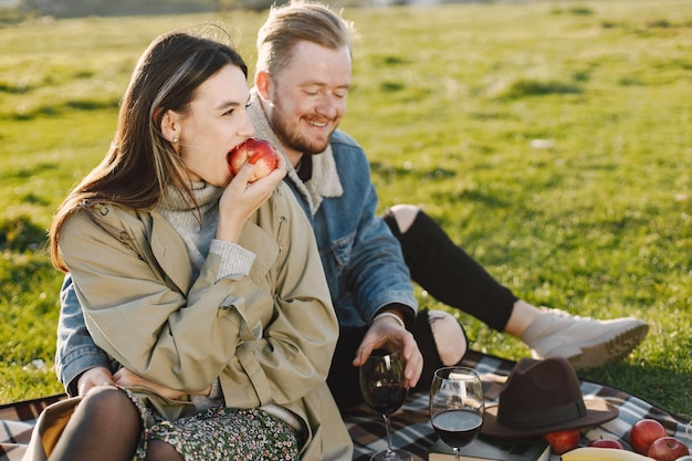 Pareja romántica en ropa de moda sentado en la naturaleza sobre una alfombra de picnic. Hombre vestido con chaqueta y abrigo de mujer