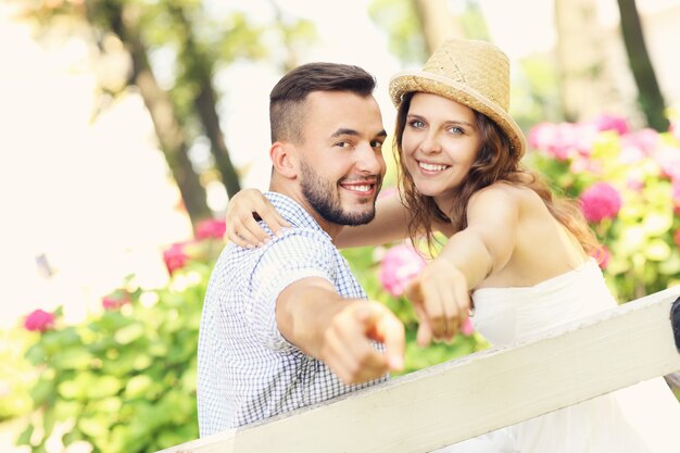 Foto una pareja romántica sentada en el parque y apuntando a la cámara.