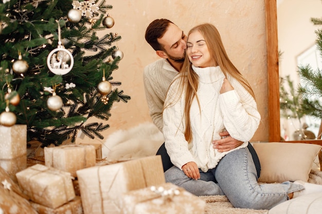 Pareja romántica sentada en un piso cerca del árbol de Navidad en casa