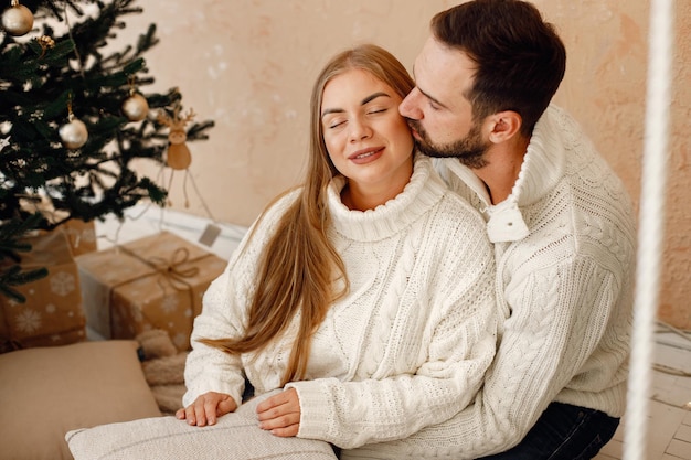 Pareja romántica sentada en un piso cerca del árbol de Navidad en casa