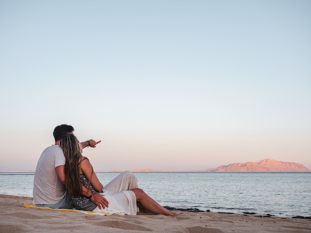 pareja romántica sentada en la playa y mirando el mar